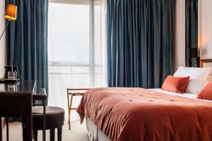 a bedroom with a bed and a desk and a window at Hotel & Spa Les Roches Noires in Les Sables-d'Olonne