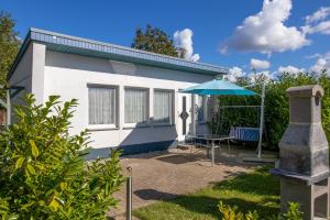 a small white house with a table and an umbrella at Bungalow am Waldrand in Barth