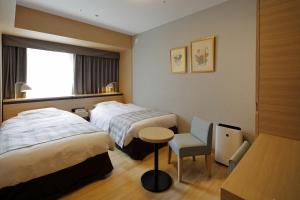 a hotel room with two beds and a table and a chair at Hotel Monte Hermana Fukuoka in Fukuoka