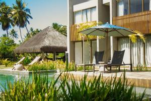 a patio with a table and an umbrella next to a building at Villa Naluri - Studio Iamandu A001 in Japaratinga