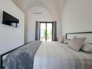 a white bedroom with a large bed and a television at Casina Pompiliano in Nardò