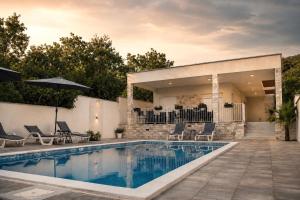 a pool with chairs and an umbrella next to a house at Villa Blanco in Mostar