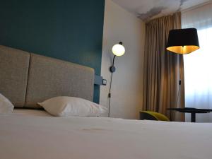 a bedroom with a bed with a white pillow and a lamp at ibis Chambery in Chambéry
