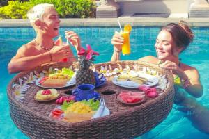 two women sitting around a table with food in a swimming pool at The Box Paradise Bungalow in Nusa Penida
