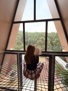 a woman reading a book in front of a window at La Estela NatureSuite in Mazamitla