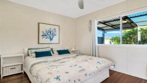 a white bedroom with a bed and a window at Frangipani Cottage in Wooli