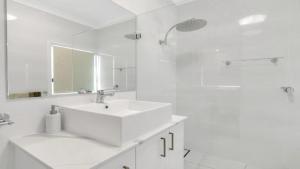 a white bathroom with a sink and a mirror at Frangipani Cottage in Wooli