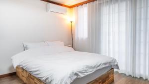 a bedroom with a bed with white sheets and a window at Geoje Blueberry Pet Pension in Geoje