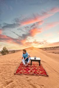 a person sitting on a rug in the desert at Royal Erg Chebbi Luxury Camp in Adrouine