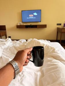 a person is holding a coffee cup on a bed at Jj Internatinals Group in Bhopal