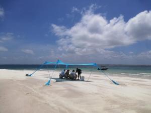 a group of people standing under a blue tent on a beach at Ayira Campsite in Vilankulo Airport