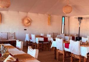 a dining room with tables and white chairs at Sahara Legacy Camp in Merzouga