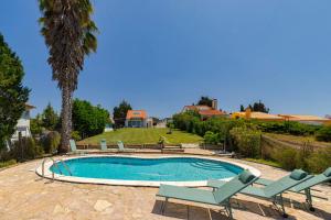 a swimming pool with two lounge chairs and a palm tree at Casa da Colina, By Home Match in Sesimbra