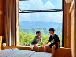 two boys sitting in a window looking out at the mountains at Black Stone Hilltop Great Wall Lodge & Whisky Lounge in Simataicun +47 photos