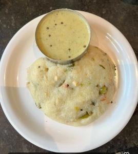 a white plate with a bowl of dipping sauce on top at VIDYA Homestay in Hampi