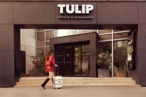 a woman walking outside of a hotel with a suitcase at Tulip Hôtels & Residences Joinville-Le-Pont in Joinville-le-Pont