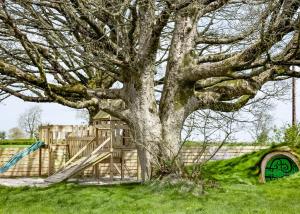 a tree with a wooden fence and a playground at Arts Hollow in Binegar