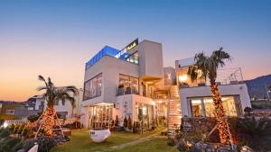 a large white house with palm trees in front of it at Seogwipo Dawa Pool Villa Pension in Seogwipo