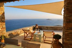 a woman sitting on a patio with a table and chairs at "GOLDEN SUNSET VILLA" 3-BDR, Breathtaking Views in Batsi