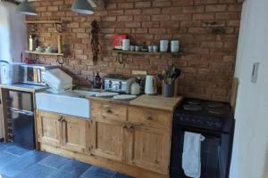 a kitchen with wooden cabinets and a brick wall at 1 Bed Barn - Sleeps 2 - Pool - Garden - Bbq in Taunton