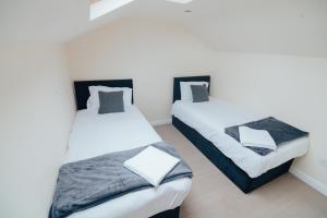 two beds in a room with white and gray sheets at The Welsh Welcome in Pen-y-groes
