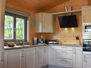 a kitchen with white cabinets and a flat screen tv at Pine Lodge - Uk30007 in Lindal in Furness