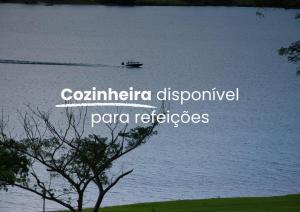 a boat on a lake with a tree in the foreground at Morro Redondo - Bangalôs com vista do lago e da serra in CÃ¡ssia