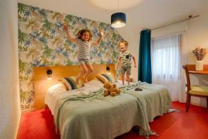 two children jumping on a bed in a hotel room at Hotel Le Branhoc - Brit Hotel Auray in Auray