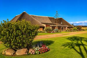 a thatch roofed house with a yard with flowers at Linglela Lodge in Estcourt