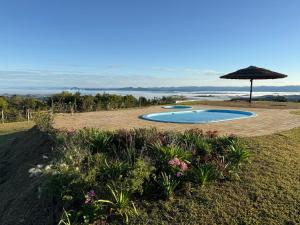 a swimming pool with an umbrella and some flowers at Sítio Paradouro in Novo Hamburgo