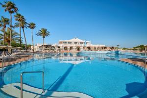 a large swimming pool with palm trees and a building at Grupotel Mar de Menorca in Es Canutells +51 photos