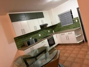 a kitchen with green tile and white cabinets and a glass table at Essie's Place in Windhoek +2 photos