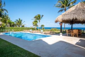 a swimming pool with chairs and a straw umbrella at Costa Brava Apartments I Ocean Front in Puerto Aventuras