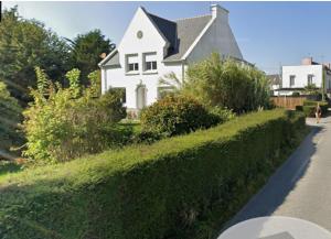 a white house on a hill with a hedge at apartement avec parking prive in Concarneau