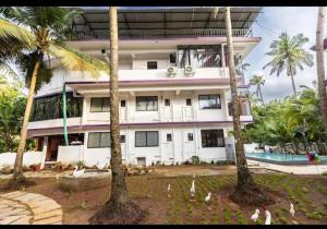 a large white building with palm trees in front of it at Colors Fly Hotel in Colva