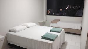 two beds in a white room with a window at Pousada Panorama Palace in Santa Maria da Vitória