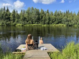 two people and a dog sitting on a dock in the water at Lapland Aurora Riverside in Raiskio