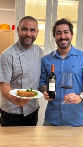 two men holding a bottle of wine and a plate of food at Pousada e Adega Lapa do Lobo in Conservatória