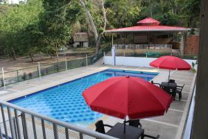 a swimming pool with two red umbrellas next to at Finca Campestre el Paraíso Resort Hotel en Mesitas in El Colegio