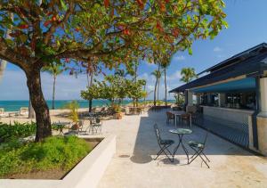 a patio with chairs tables and a tree and the beach at Blue Coast Condo in Puerto Plata