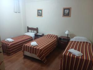 three beds in a hotel room with striped sheets at Pousada Narcizo in São Lourenço