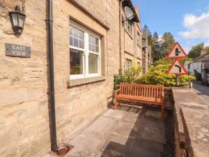 a wooden bench next to a building with a street sign at East View in Kirkby Stephen