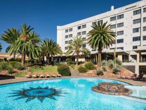 a swimming pool in front of a hotel with palm trees at Mövenpick Hotel Windhoek in Windhoek