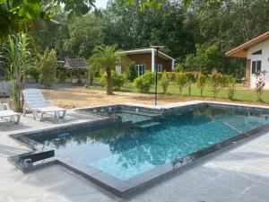 a swimming pool in a yard with two chairs and a house at Noi’s Paradise Homestay in Phatthalung