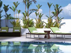 a pool with two lounge chairs and a table next to a swimming pool at Pullman Kuching in Kuching