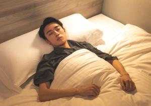 a man laying in a bed under a pillow at Super Hotel Inn Kurashiki Mizushima in Kurashiki