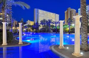 a pool with palm trees and buildings at night at SOL by Meliá Pelícanos Ocas in Benidorm
