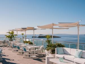 a patio with white tables and chairs and the ocean at MiM Ibiza member of Meliá Collection in Ibiza Town