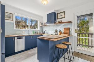 a kitchen with blue cabinets and a counter with stools at Gunyha - Ocean Views, Walk to Beach, Free WiFi, Pet Friendly, Open Fire, Visiting Koalas and Other Wildlife. in Apollo Bay