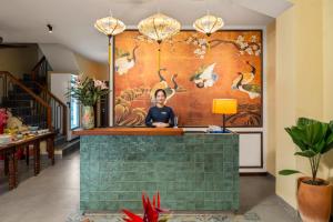 a woman sitting at a counter in a room with a mural at Solea Boutique Hoi An - Grand Opening April 2026 in Hoi An